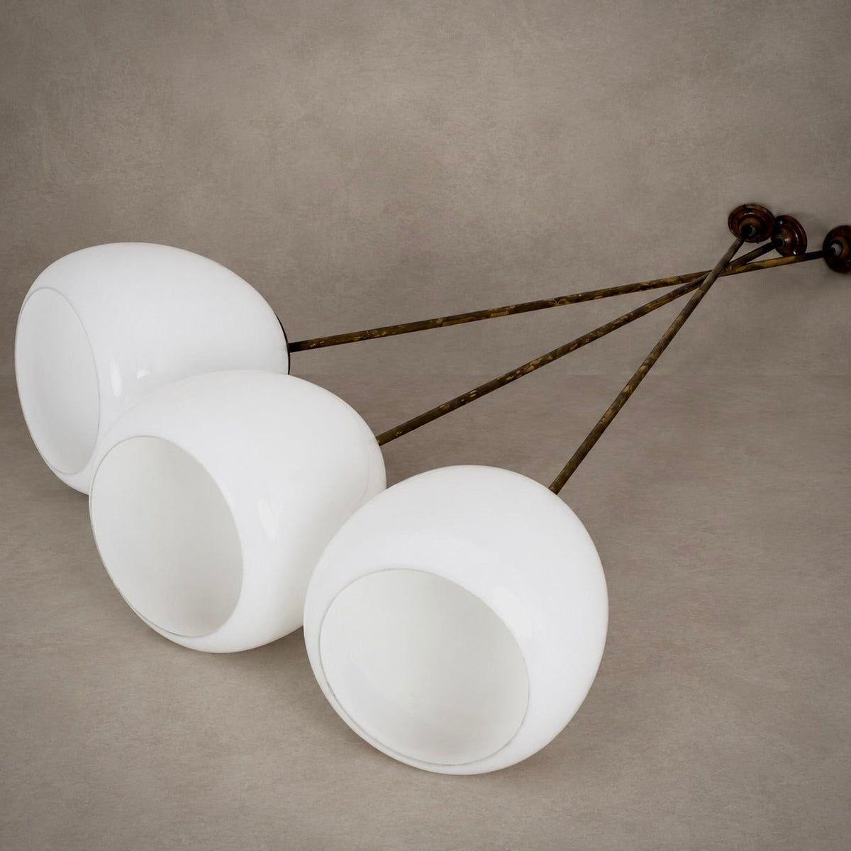 Three white spherical pendant light shades suspended from a dark metal frame against a textured beige background.