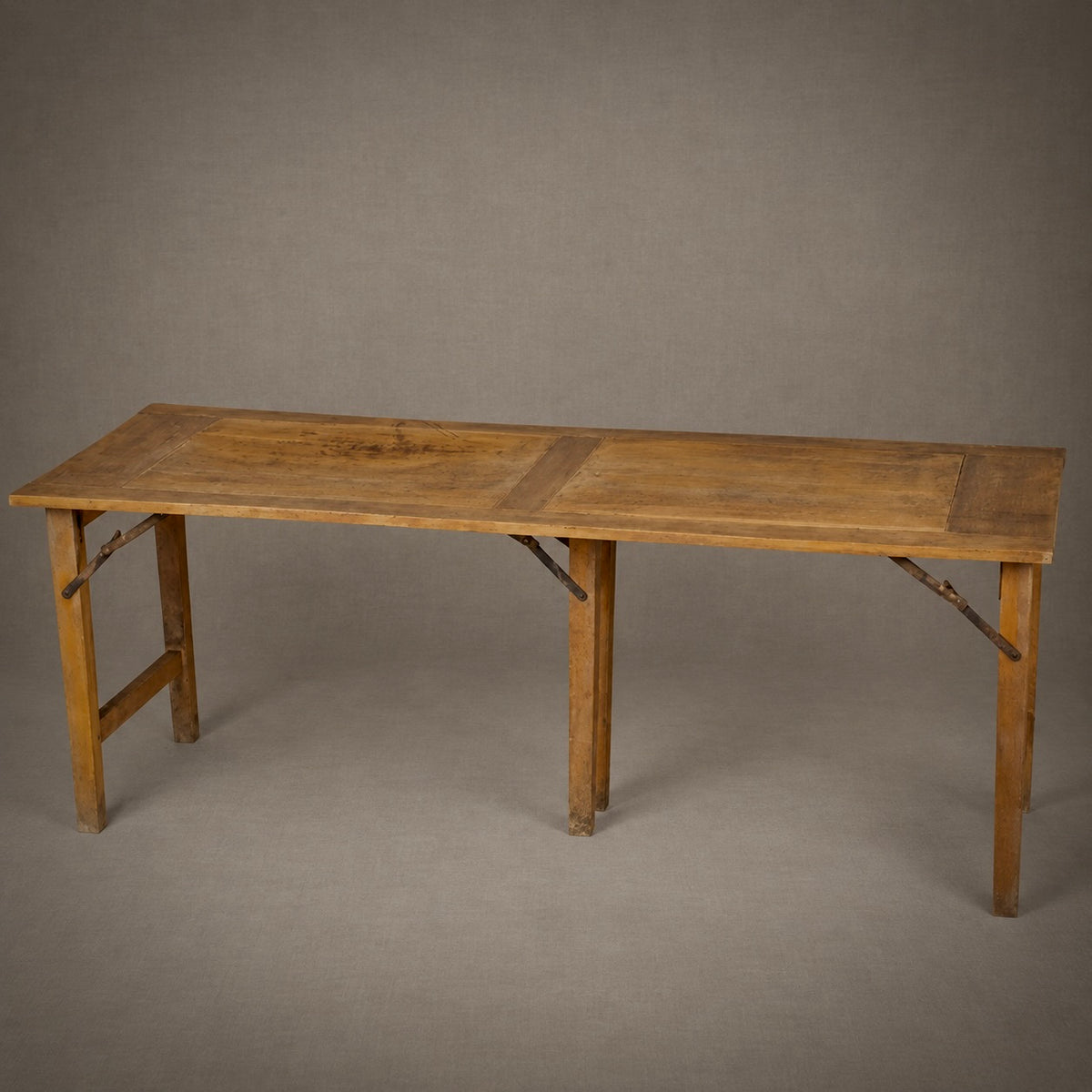 A rustic wooden folding table with a warm medium-brown finish, shown against a neutral gray studio background.