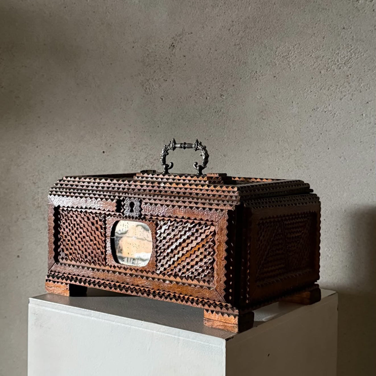 A carved wooden decorative box with intricate geometric patterns and a small oval window, displayed on a white pedestal against a textured gray wall. The dimensions '32x22x17cmh' are printed in the bottom-left corner.