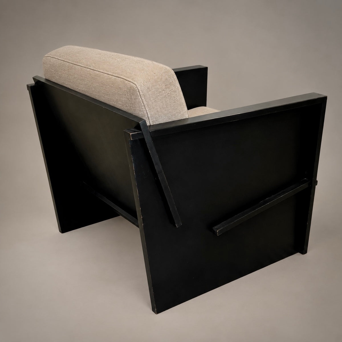A modern black wooden armchair with a light beige textured fabric seat cushion, photographed from an elevated angle against a neutral gray studio background.