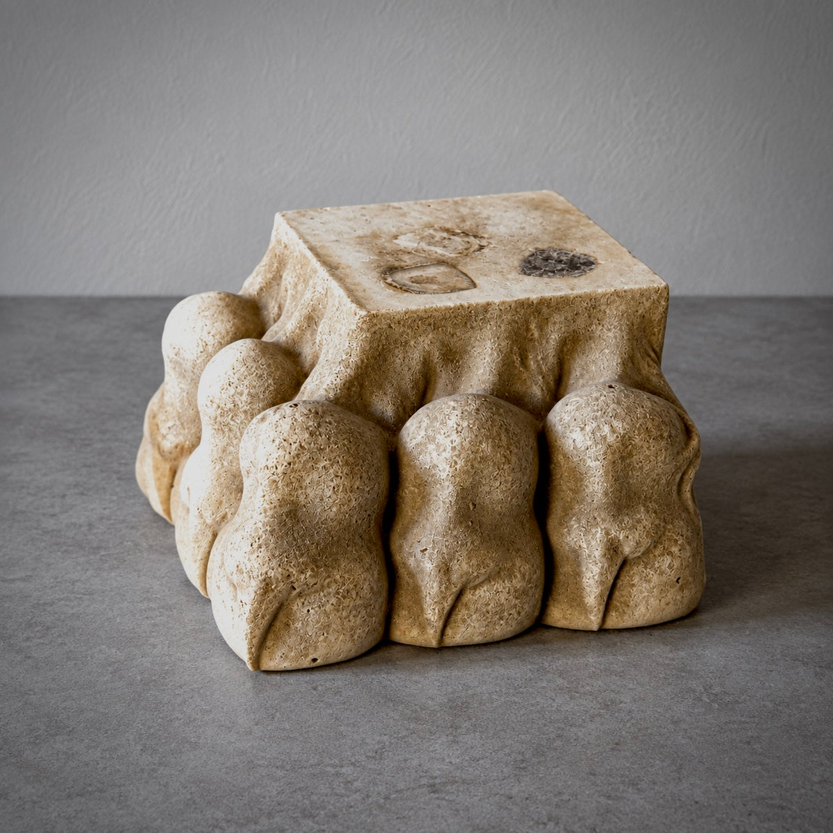 A sculptural stone lions paw with a square top and rounded, organic legs, photographed on a gray tabletop against a gray wall.