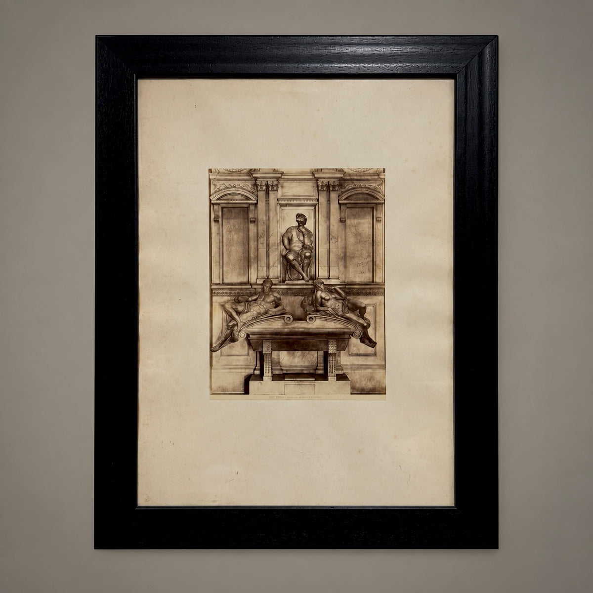 A framed sepia-toned architectural sketch or print mounted on a cream mat, enclosed in a black frame against a neutral gray wall.