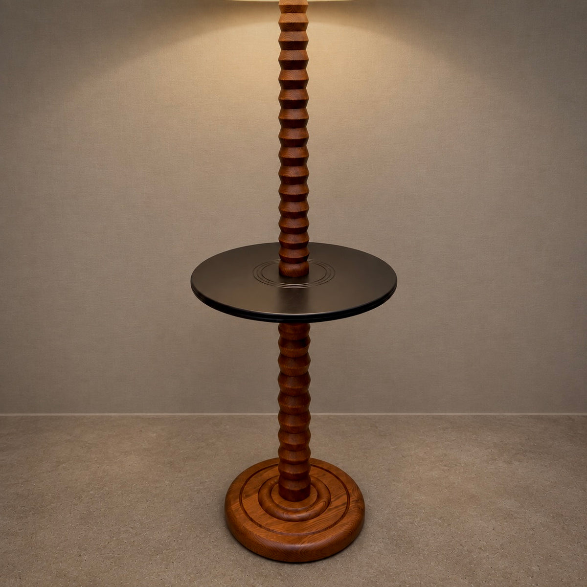 A unique floor lamp with a circular black side table in the center, supported by two twisted wooden pillars that extend from a round wooden base, set against a neutral gray wall and floor.