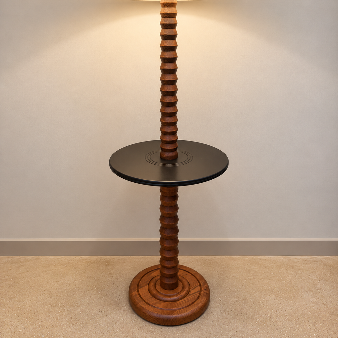 A vintage-style floor lamp with a tall, ribbed wooden pole, a round black side table in the middle, and a large beige fabric drum shade, shown lit against a neutral wall.