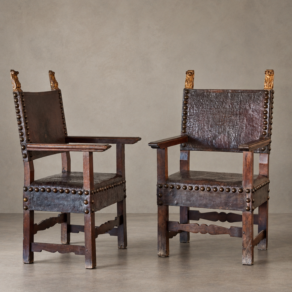 A pair of baroque style armchairs with carved walnut wood frames, hand-painted gilt detailing, and burnished leather seats
