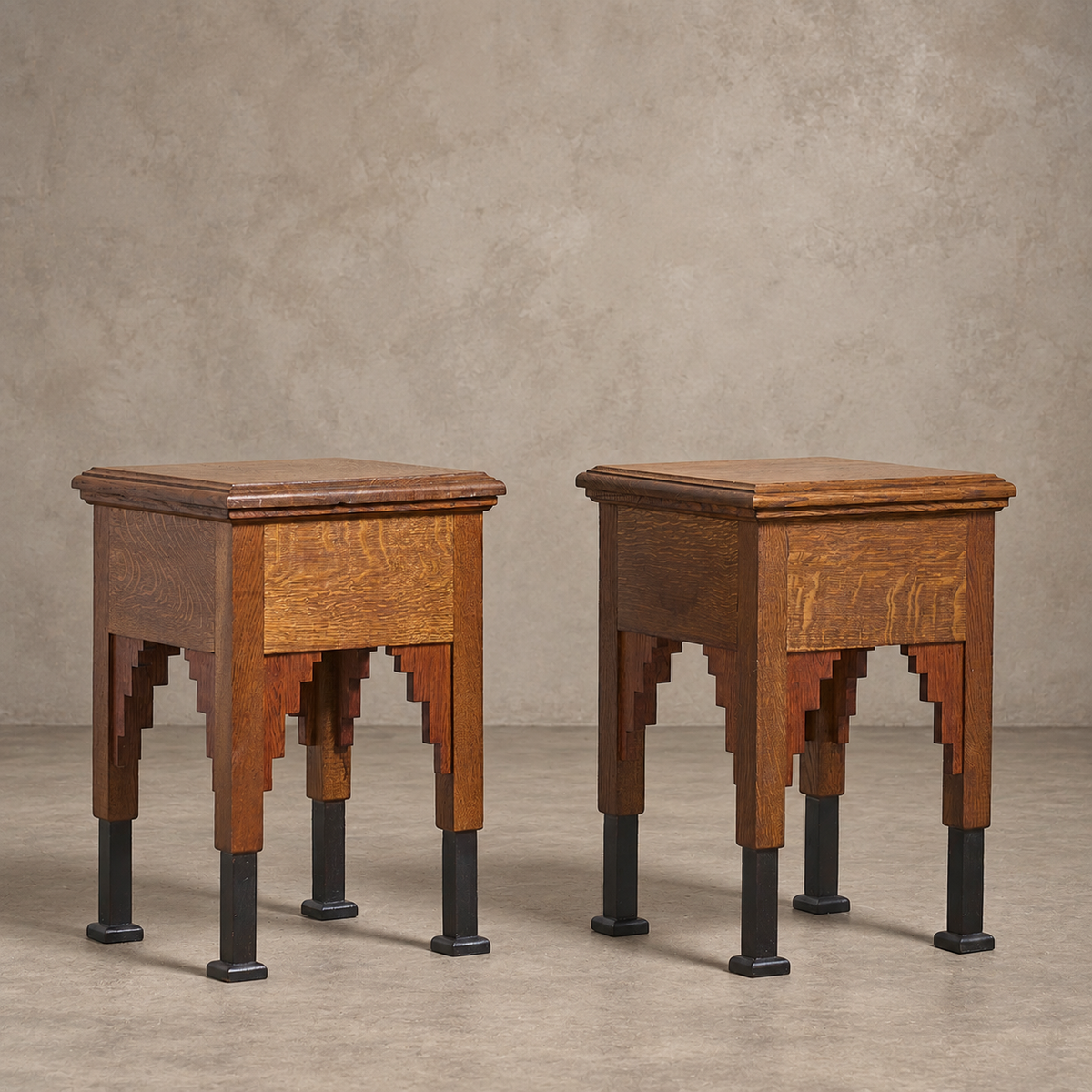 Two matching mid-century wooden side tables with geometric stepped legs and black metal feet, set against a textured beige wall and concrete floor.