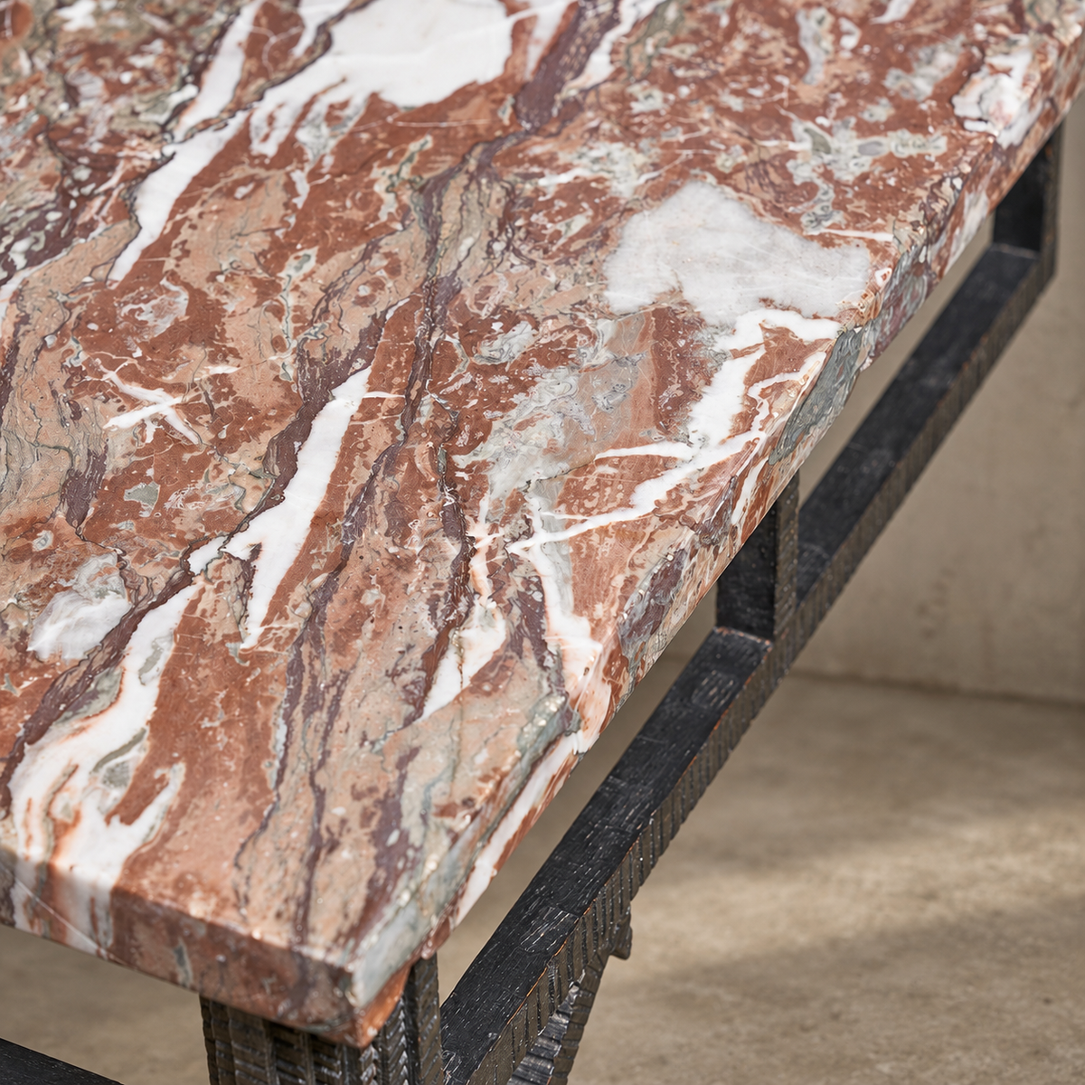 Close-up of a rectangular table with a polished reddish-brown and white marble top, supported by a dark metal frame.
