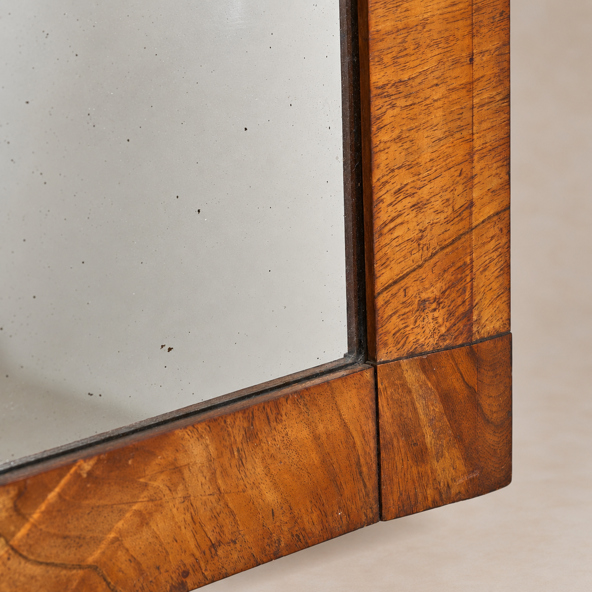 Close-up detail of a wooden mirror frame with a warm medium-brown wood grain finish and a square mirror surface.