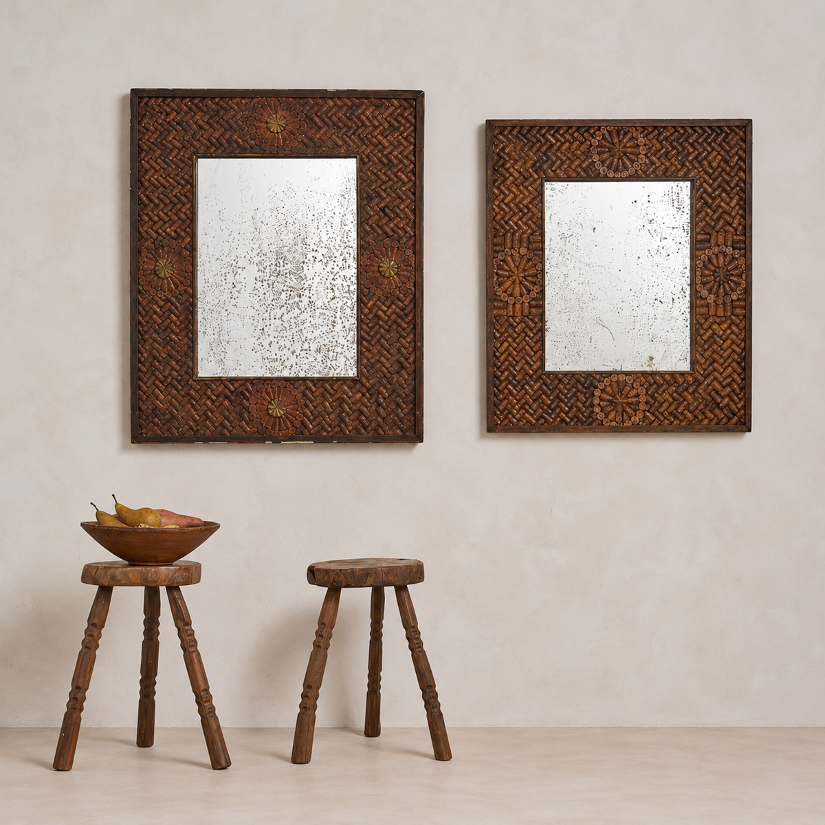 Two rectangular decorative mirrors with ornate carved dark brown wooden frames hang on a textured beige wall above two small wooden stools.
