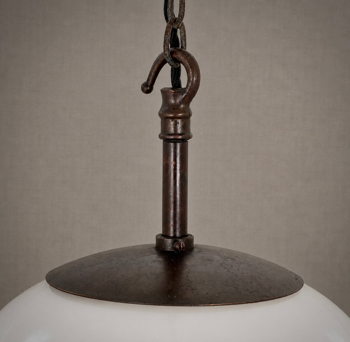 Close-up of a hanging pendant light fixture with a dark bronze metal collar, chain, and hook, attached to a white glass shade against a neutral beige background.