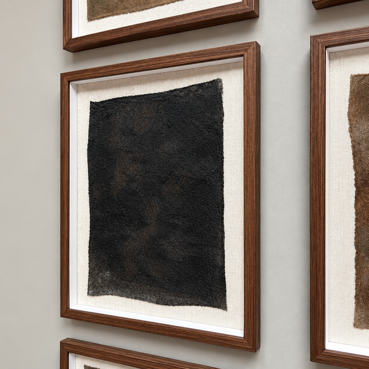 A framed abstract art print featuring a textured black rectangular panel on a cream linen background, housed in a medium brown wooden frame and mounted on a light gray wall.