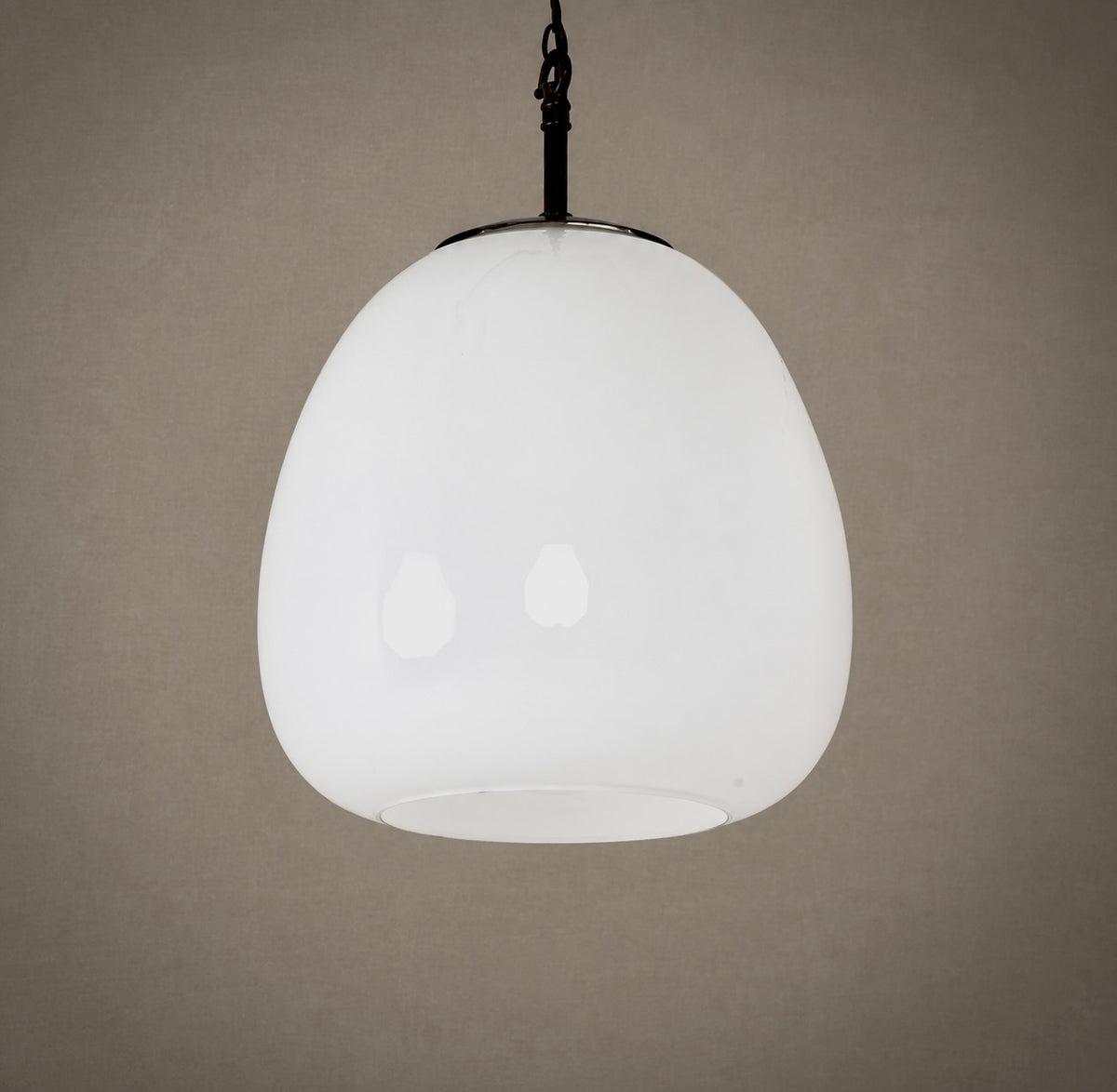 A modern pendant light with a large, rounded, opaque white glass shade suspended from a black metal rod against a textured taupe background.