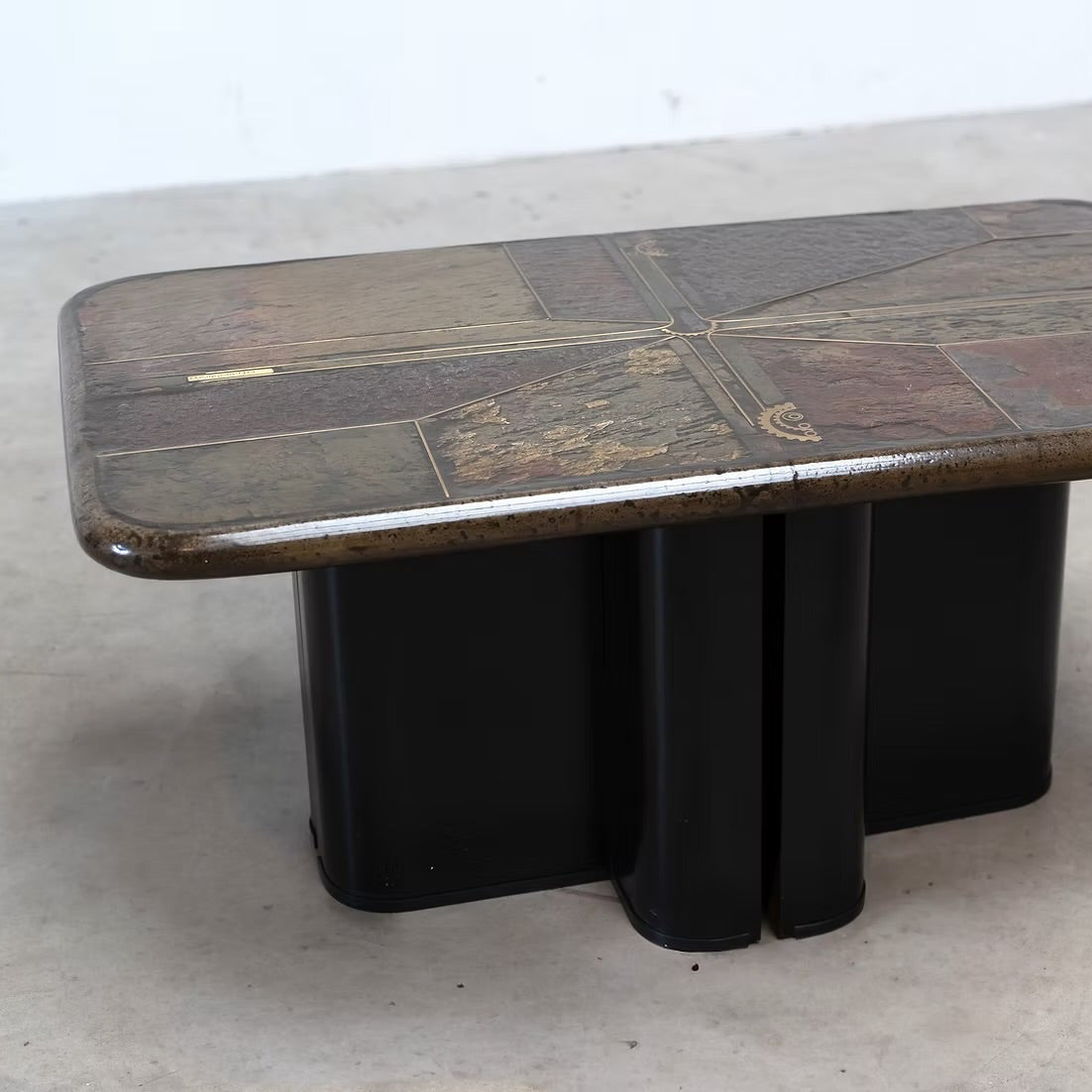 A vintage mid-century modern coffee table with a dark wood inlay top and a black metal pedestal base, photographed on a concrete floor.
