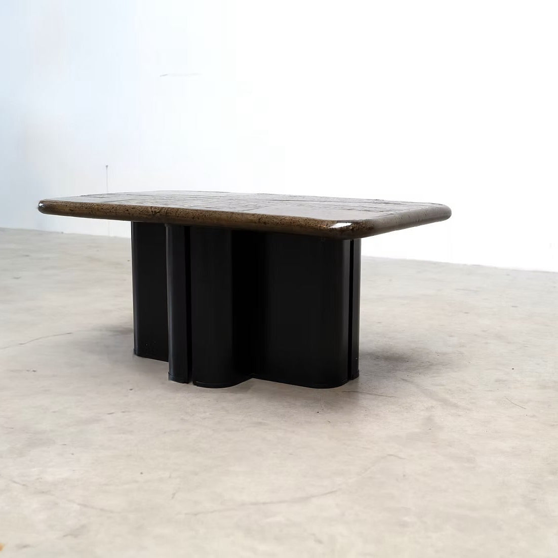 A mid-century modern low coffee table with a dark brown wood top and a black metal base, photographed in a minimalist studio setting with a concrete floor and white wall.