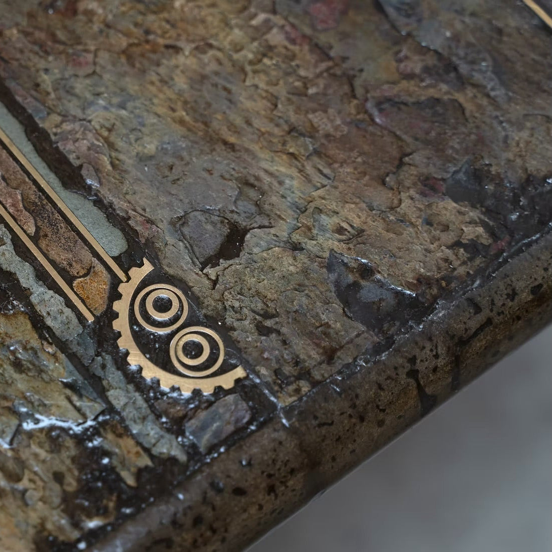 Close-up of a textured stone or concrete surface with a small brass gear detail and decorative linear accents.