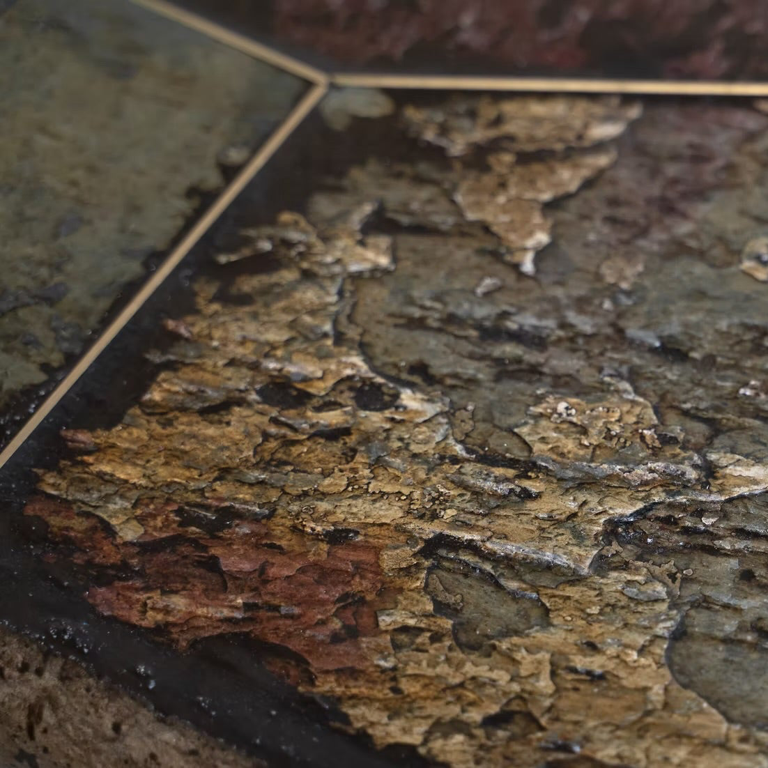 A close-up of a polished stone tile with a textured, peeling surface showing earthy tones of brown, gold, and dark gray, bordered by thin gold lines.