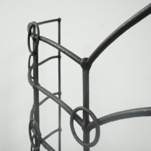 Close-up of a dark metal garden trellis or stake frame with circular and curved support bars against a plain light background.