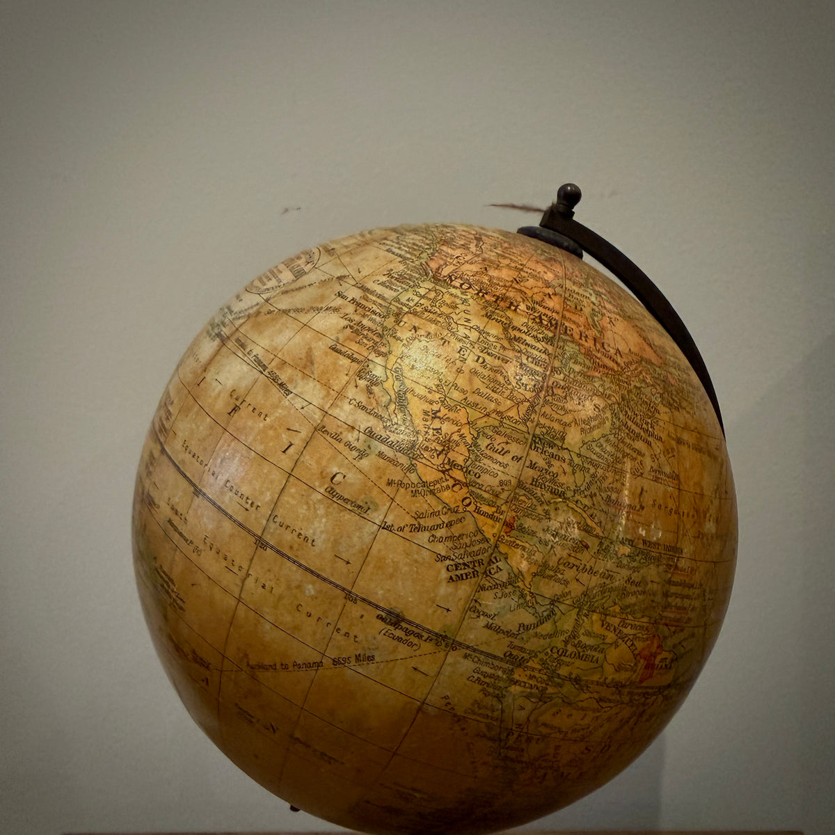 An antique-style globe with a warm tan and brown map print, supported by a black metal stand against a plain light gray wall.