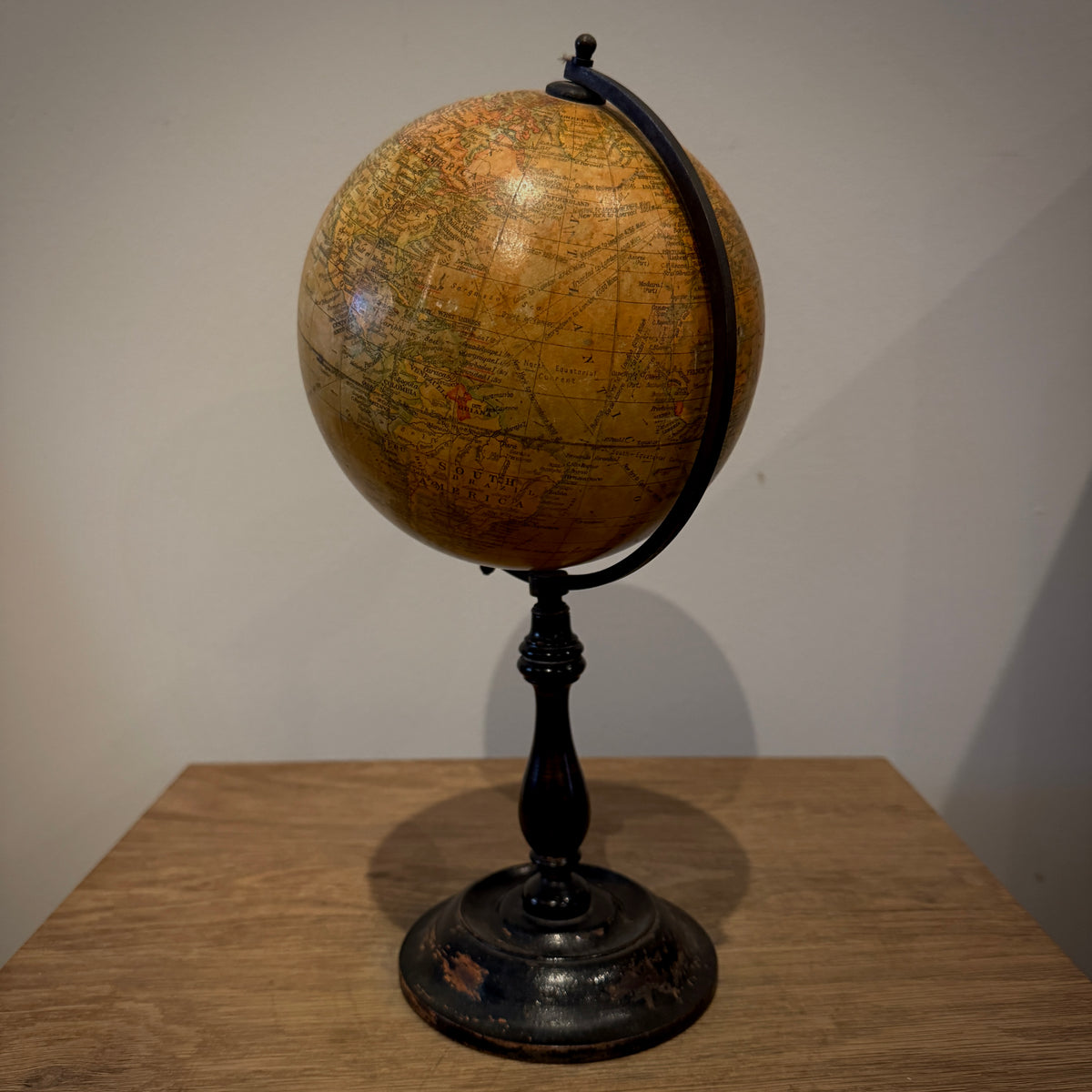 An antique-style globe on a black metal stand, displayed on a wooden table against a plain light gray wall.