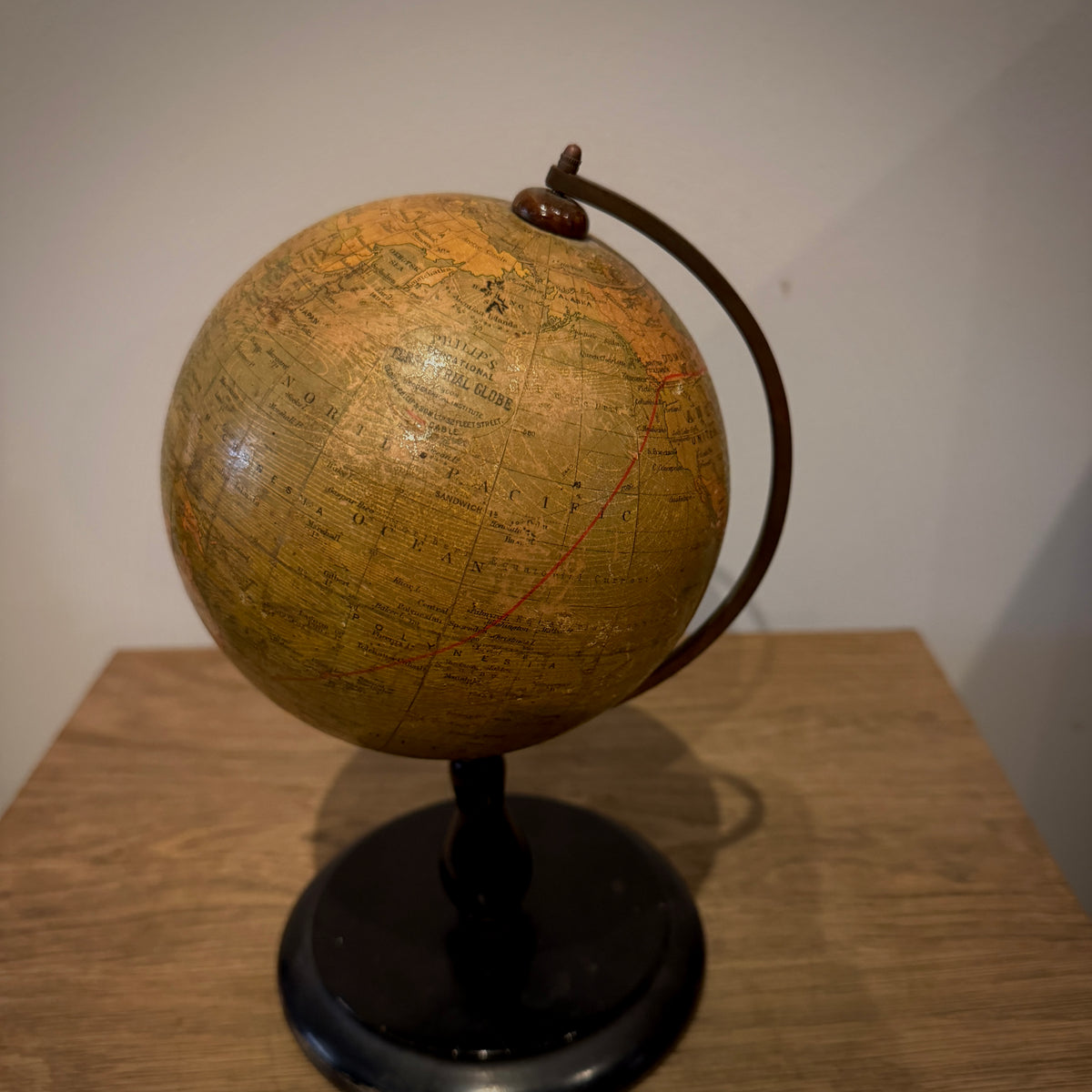 An antique-style globe with a yellowed map surface, dark brown meridian ring, and black stand, displayed on a wooden table against a plain wall.