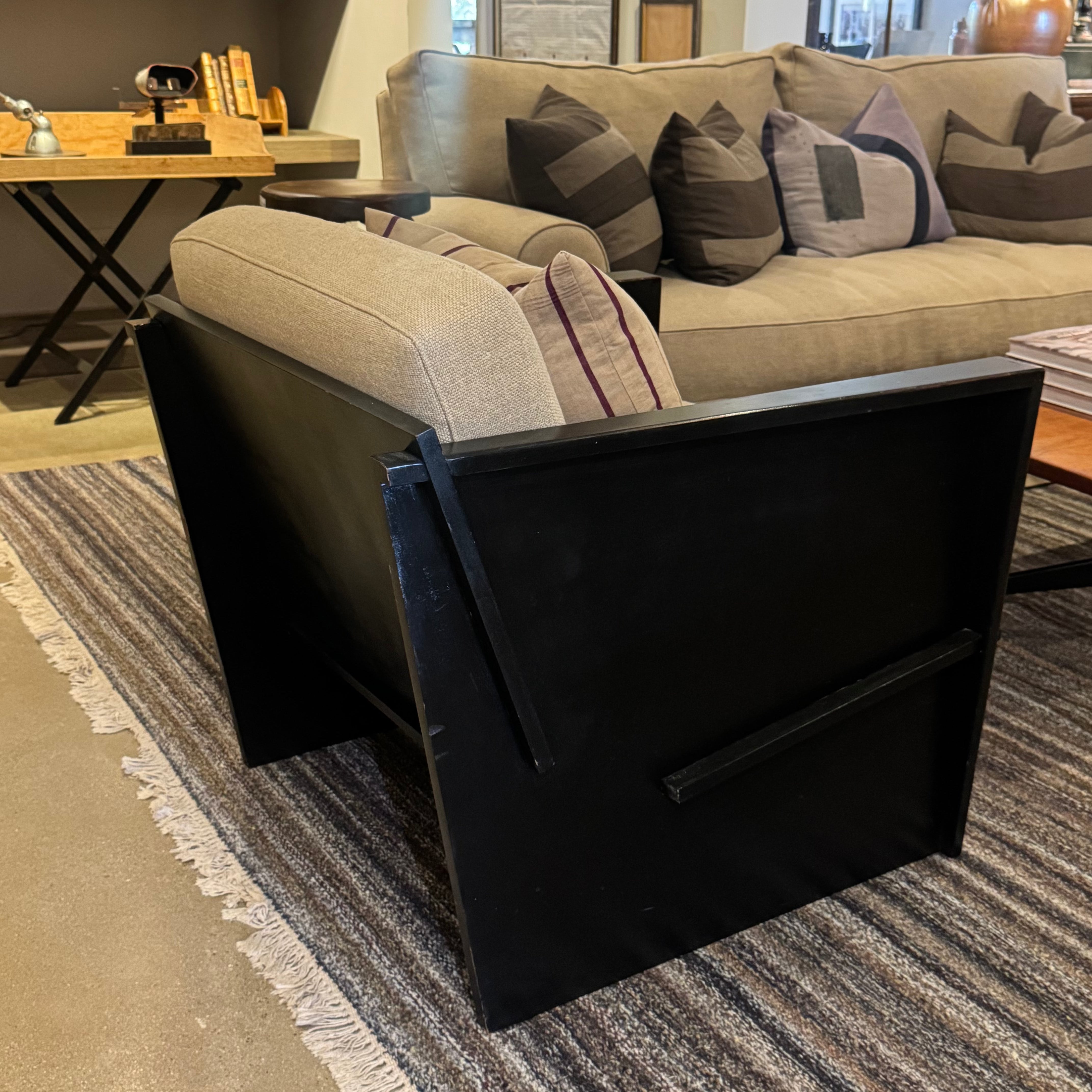 A modern black armchair with a light beige upholstered back and seat, styled in a living room setting on a striped rug next to a beige sofa.