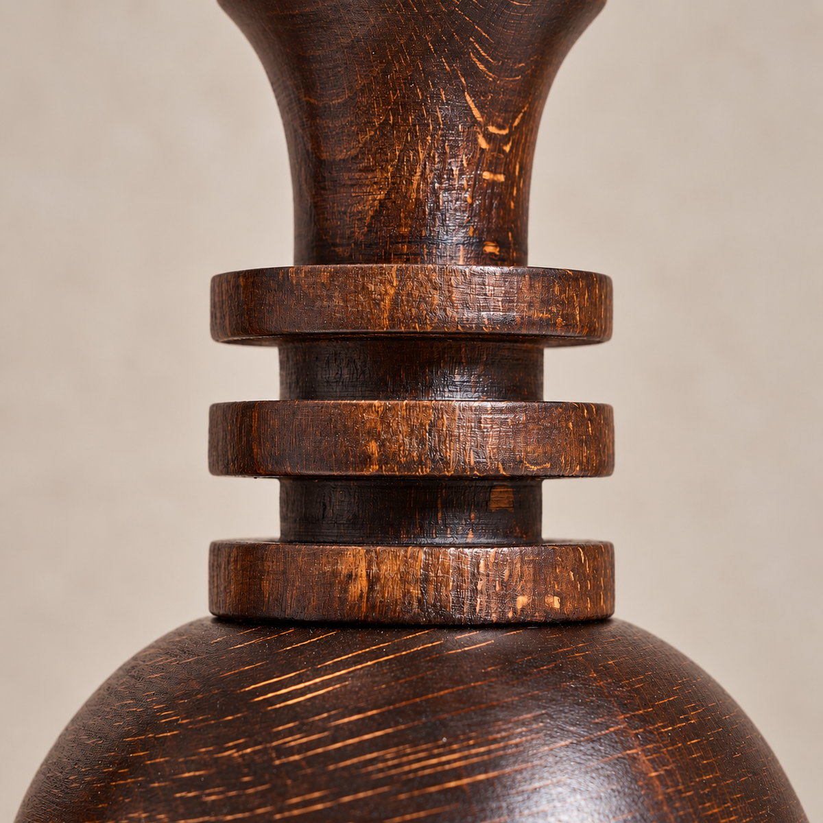 Close-up of a dark brown wooden candlestick with a rounded base, stacked ring-like bands, and a flared neck, shown against a plain beige background.