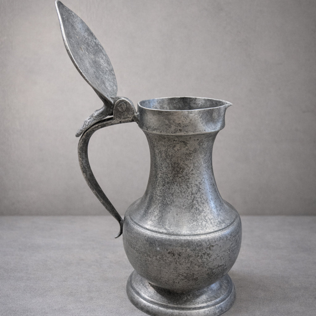 Vintage metal pitcher with a leaf-shaped handle on a gray background