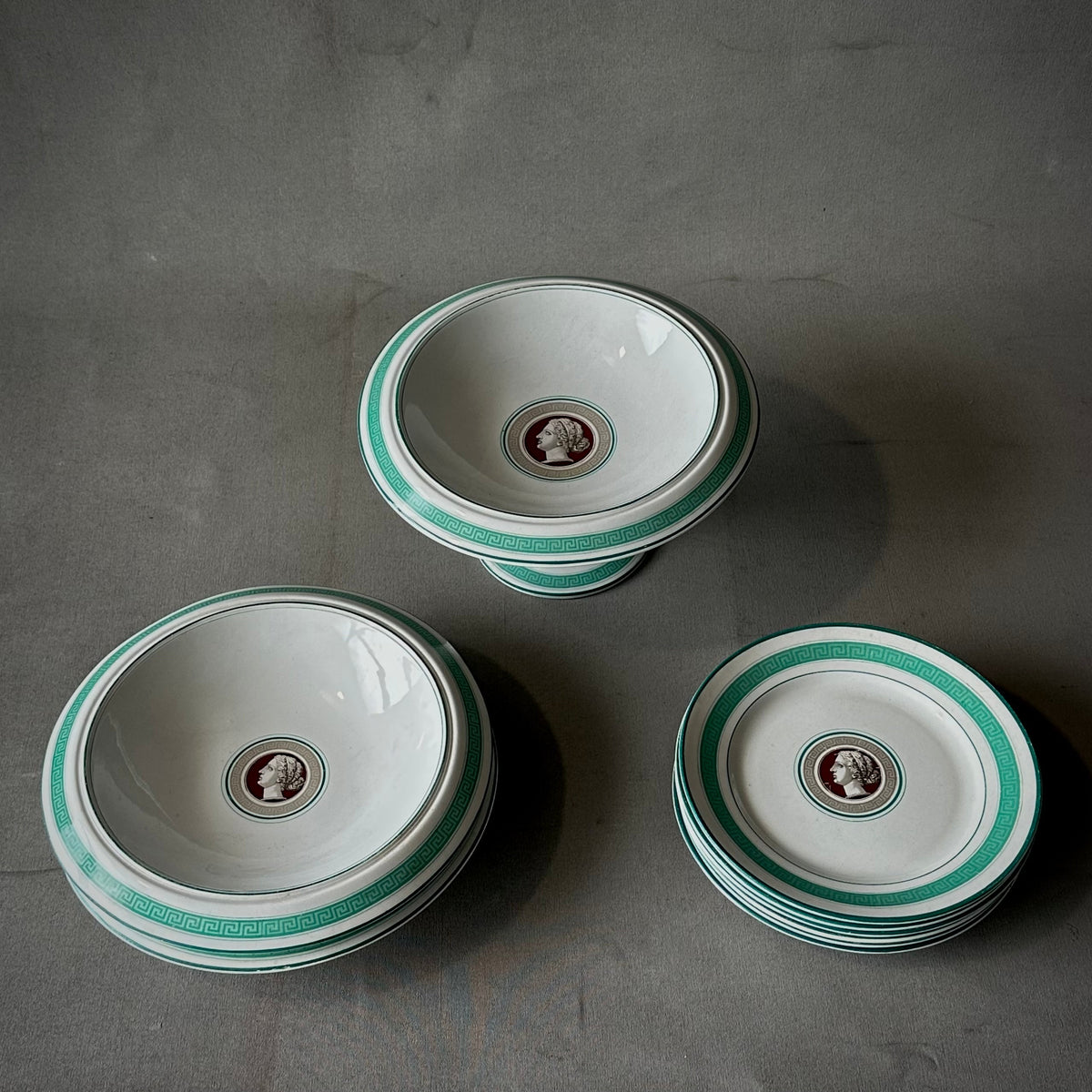 A set of porcelain dishes with a Greek key design and a medallion of a female bust in profile on each dish, featuring aquamarine trim.
