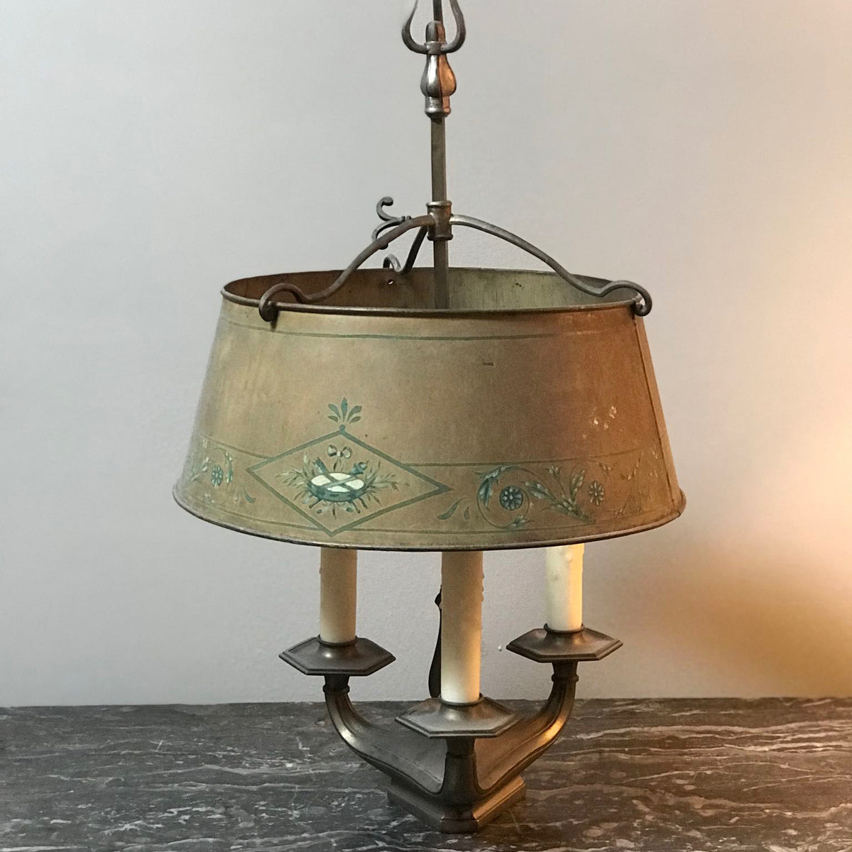 A vintage three-light metal pendant chandelier with a tapered drum shade decorated with a painted blue-green floral and bird motif. The fixture has a weathered bronze finish and is shown lit against a neutral background.