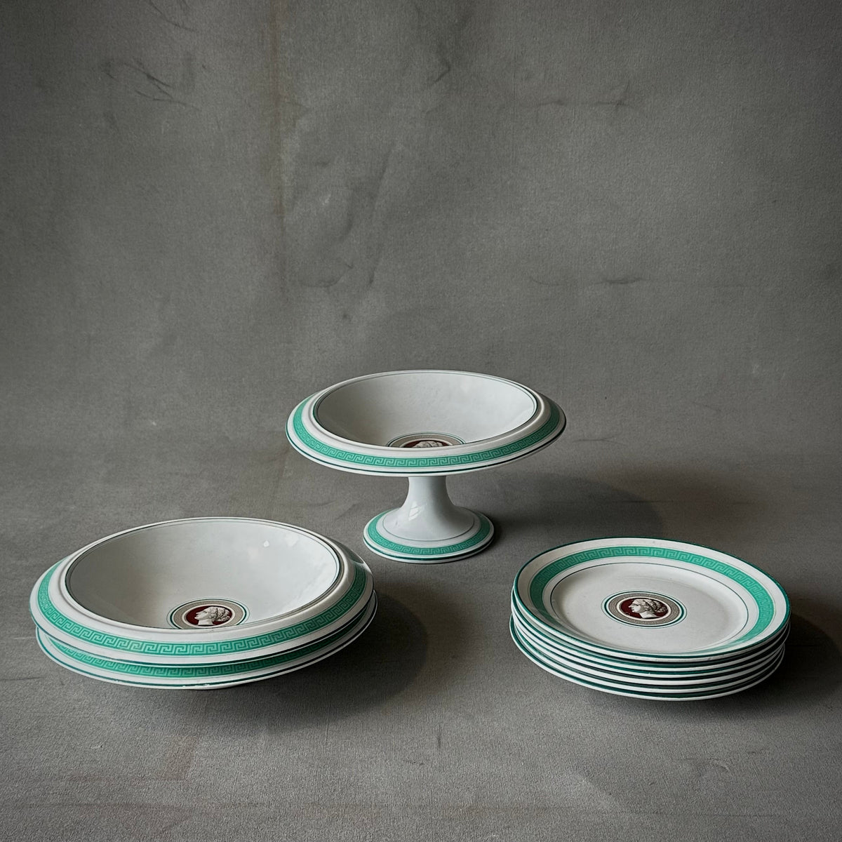 A set of porcelain dishes with a Greek key design and a medallion of a female bust in profile on each dish, featuring aquamarine trim.