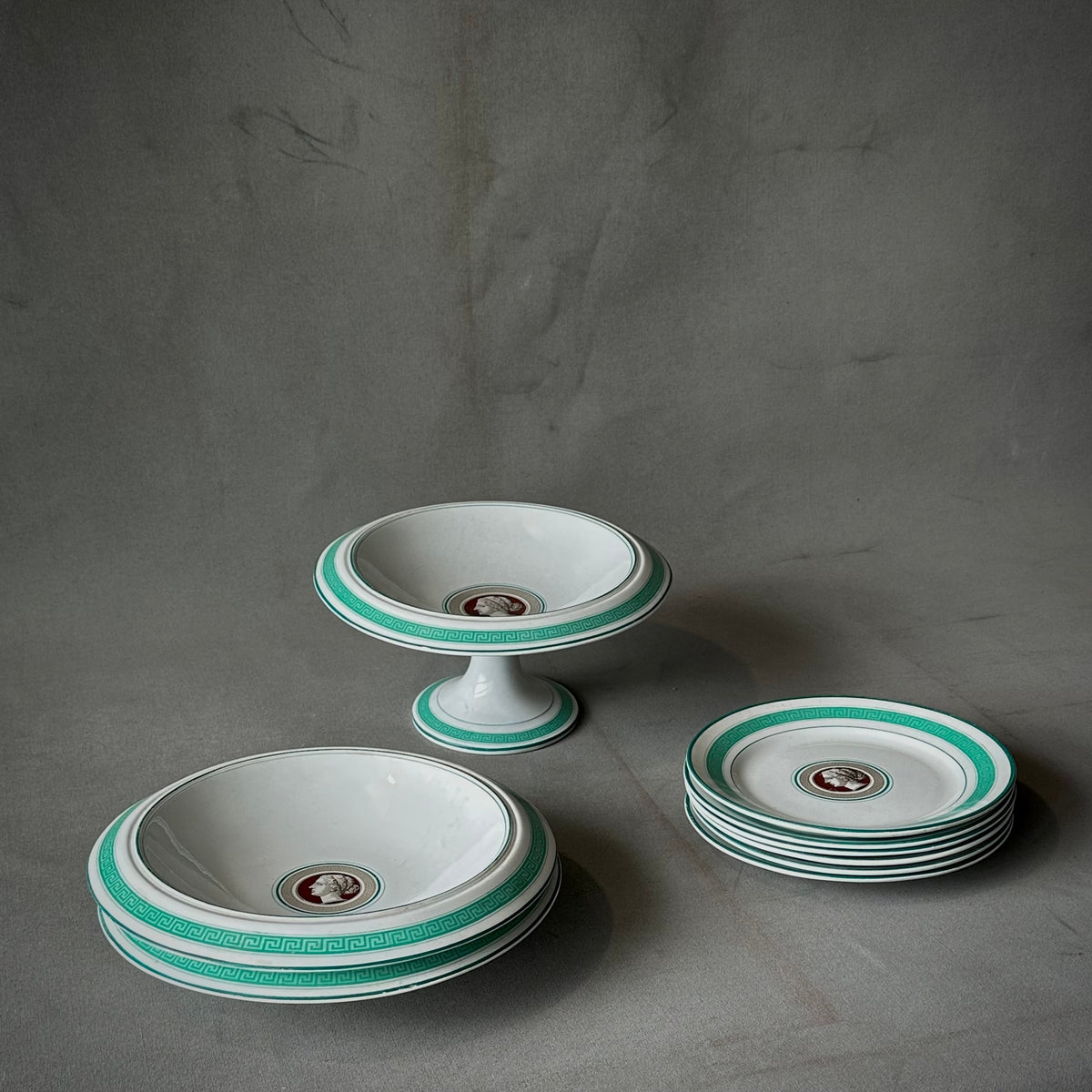 A set of porcelain dishes with a Greek key design and a medallion of a female bust in profile on each dish, featuring aquamarine trim.