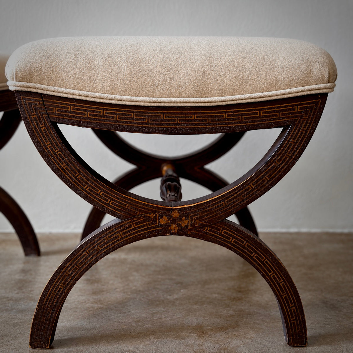 A dark brown wooden bench with an upholstered cream seat cushion, featuring geometric inlay details on the frame and curved legs.
