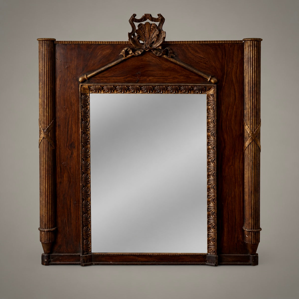 An early French mirror with carved and gilt wood, painted faux bois accents, reeded columns with conical finial bases, and a palmette motif gracing the border. A detailed carved shell crowns the pediment.