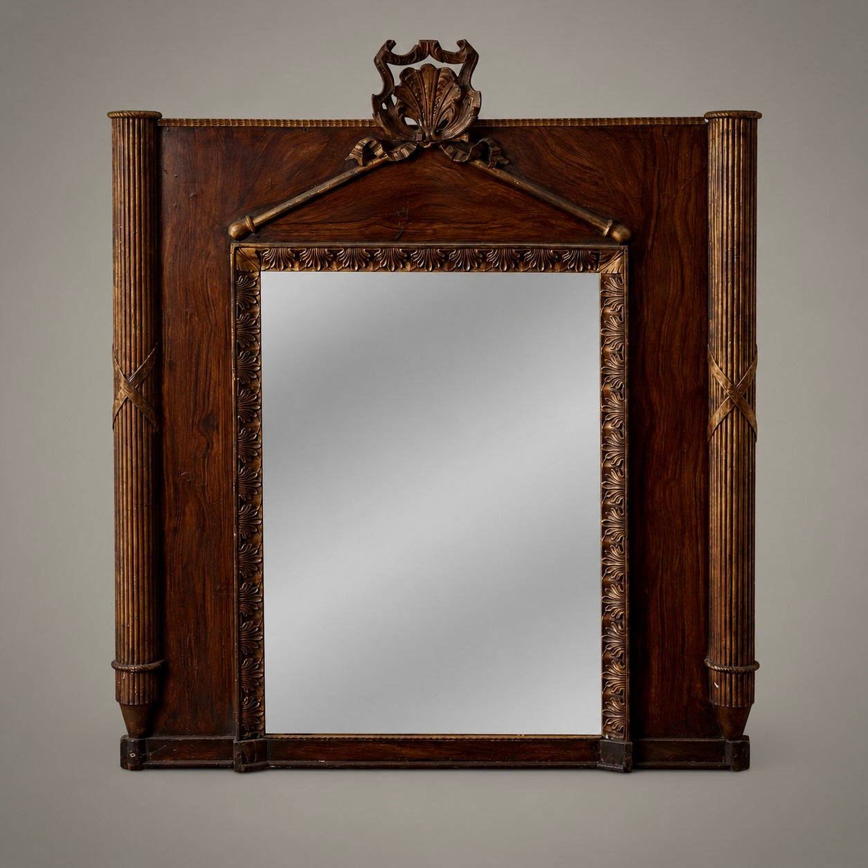 An early French mirror with carved and gilt wood, painted faux bois accents, reeded columns with conical finial bases, and a palmette motif gracing the border. A detailed carved shell crowns the pediment.
