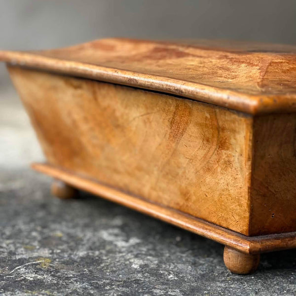 A close-up of a rectangular wooden box with a hinged lid, resting on a textured gray stone surface.