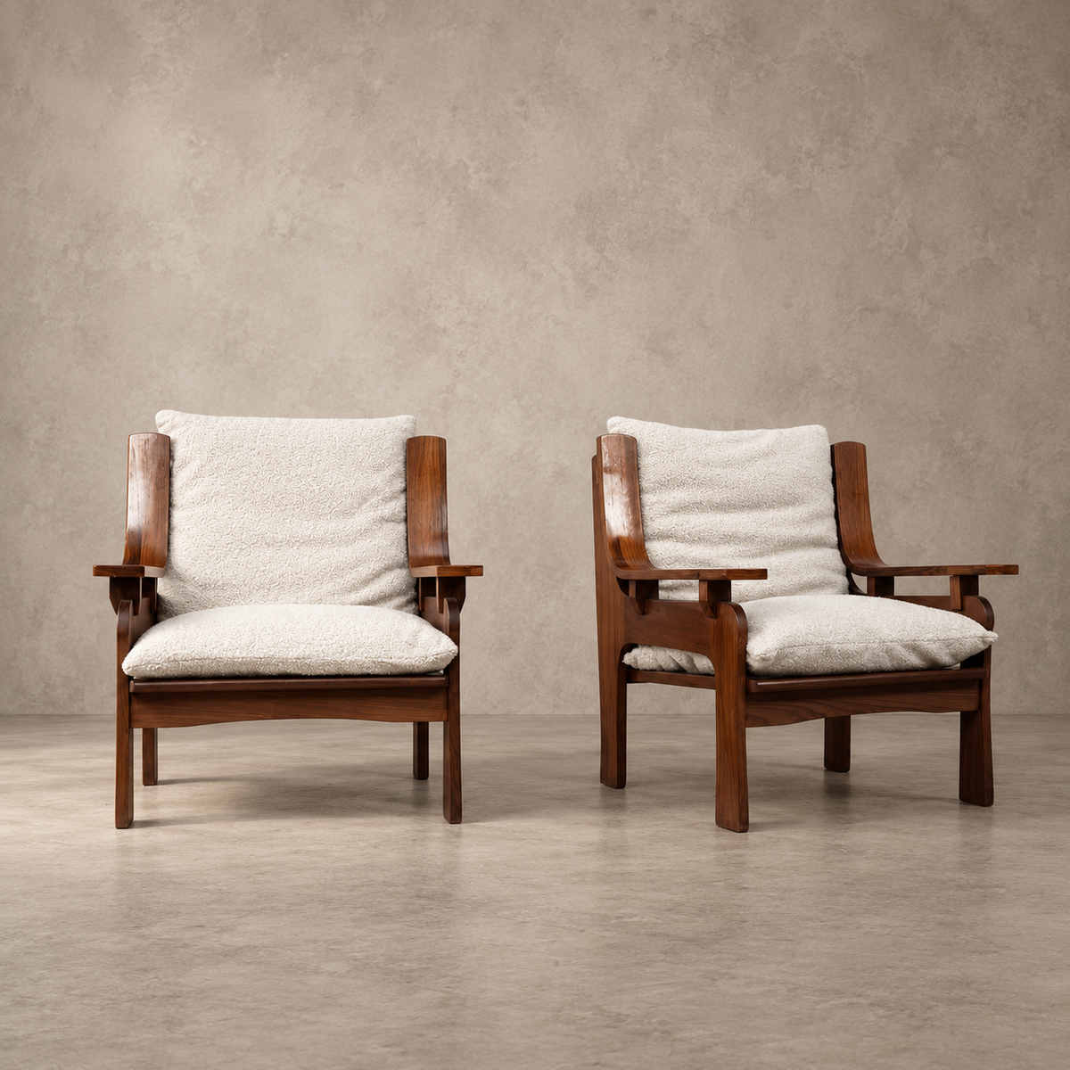 Two mid-century modern wooden armchairs with cream bouclé cushions, set against a textured concrete wall and floor.