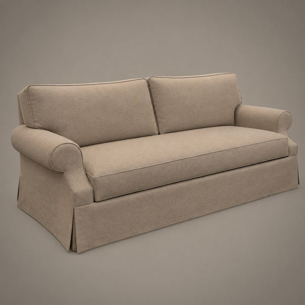 A beige upholstered sofa with rolled arms, two back cushions, and a skirted base, shown on a plain warm gray studio background.
