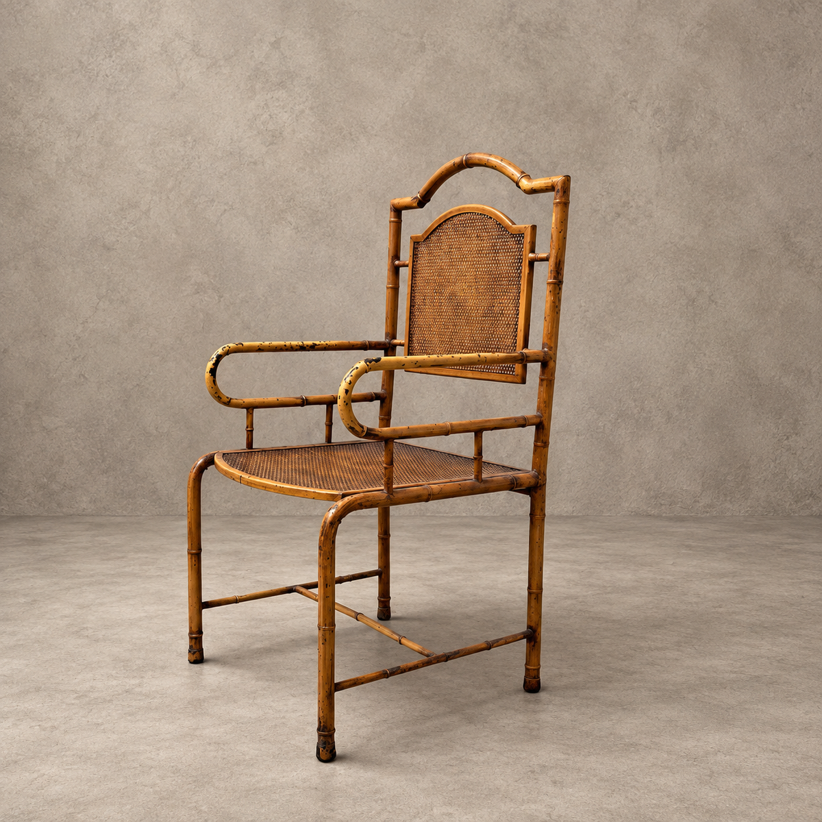 A vintage-style bamboo armchair with a woven cane seat and backrest, set against a textured gray concrete background.