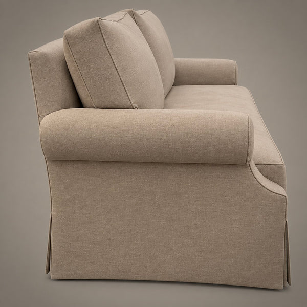 A beige upholstered sofa shown from a three-quarter side angle against a solid taupe-gray studio background.