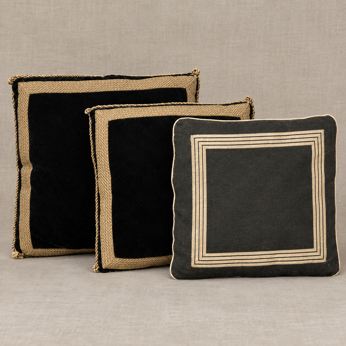 A antique black wool cushion. with woven tan borders and two velvet braided trim pillows and a charcoal cushion with geometric cream stripe detailing.