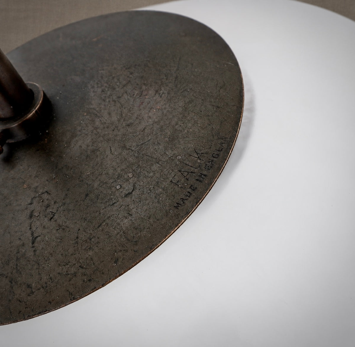 Close-up of a dark round metal lamp base with a visible maker's mark reading 'FAUX MADE IN HEBRON' on a white surface.