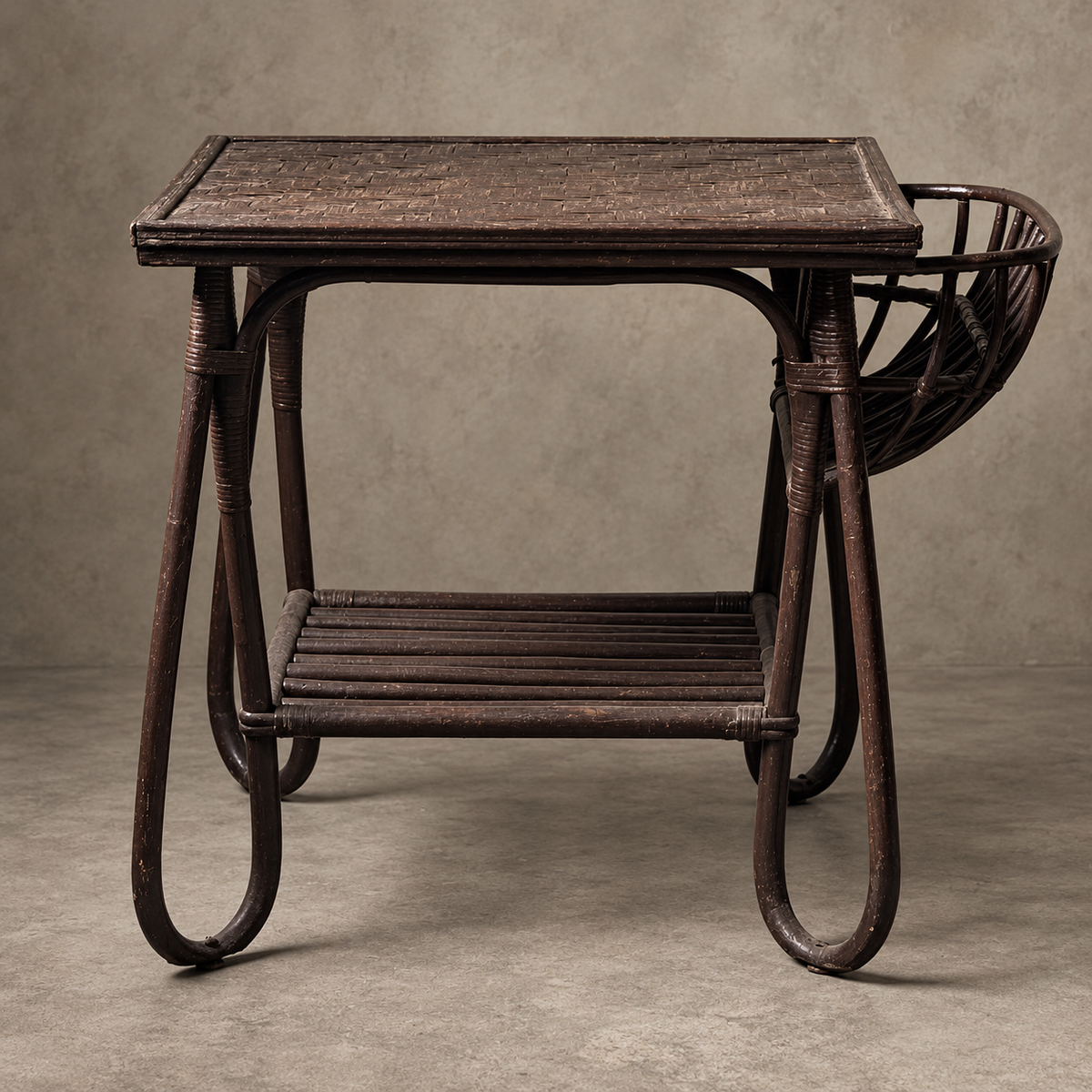 A dark brown wicker side table with a rectangular top, a lower slatted shelf, and a curved backrest, photographed against a neutral textured gray studio backdrop.