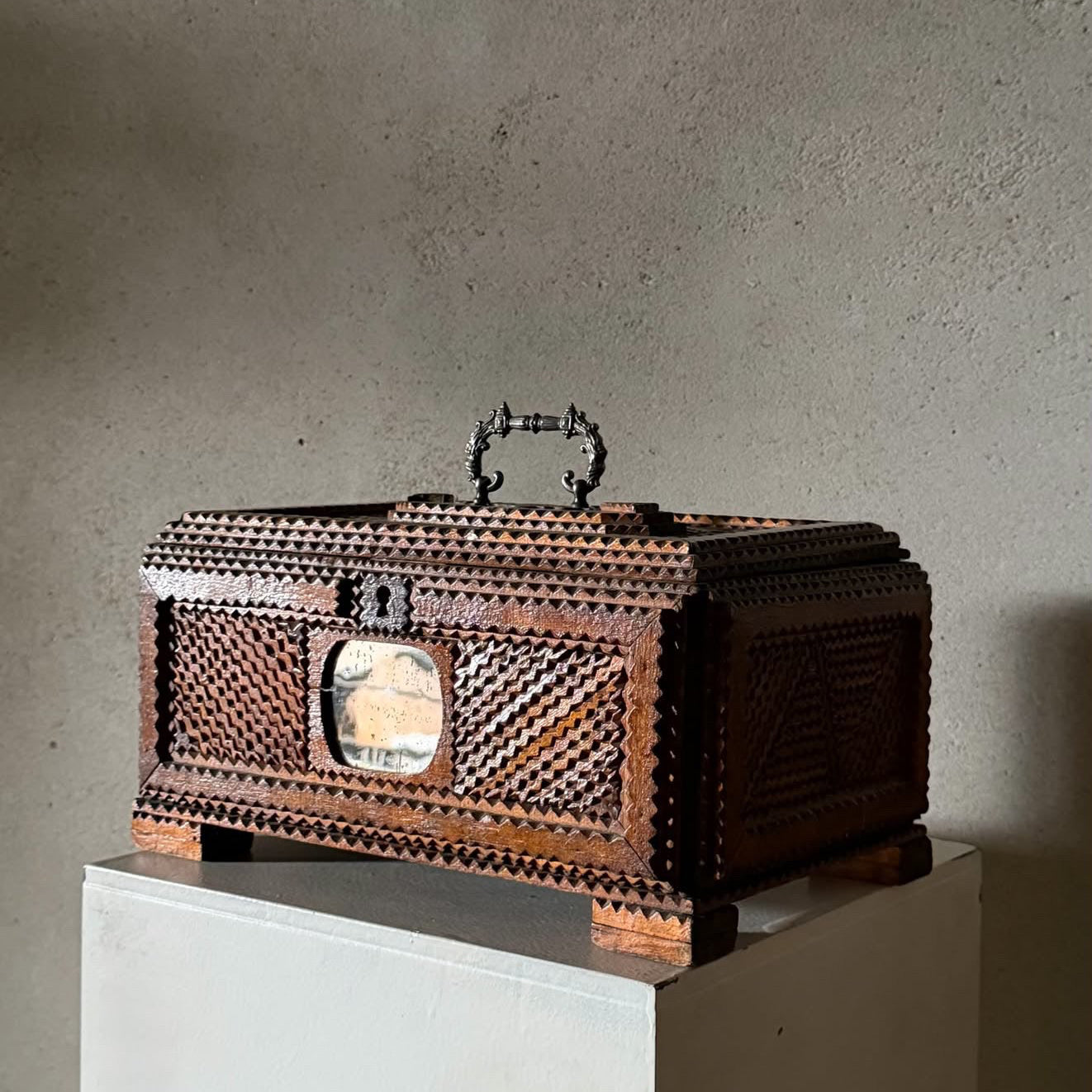 A carved wooden decorative box with intricate geometric patterns and a small oval window, displayed on a white pedestal against a textured gray wall. The dimensions '32x22x17cmh' are printed in the bottom-left corner.