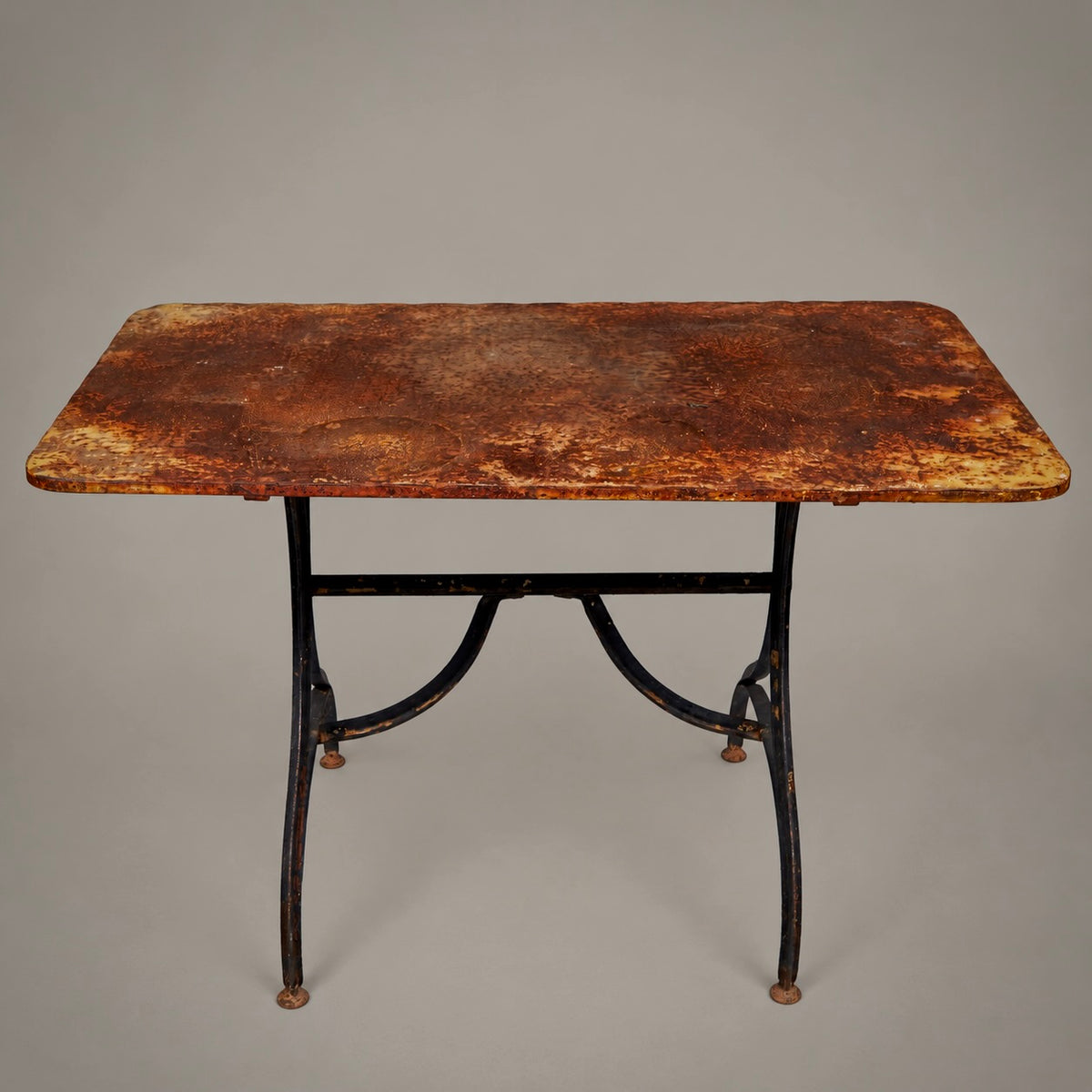 A vintage rectangular table with a distressed, rusted brown metal top and a black metal frame with curved legs, shown against a neutral gray background.