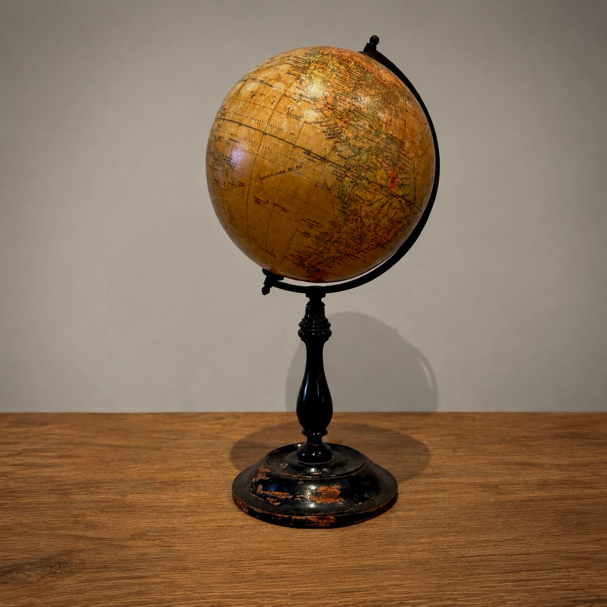 A vintage-style globe on a black metal stand, placed on a wooden tabletop against a plain light gray wall.