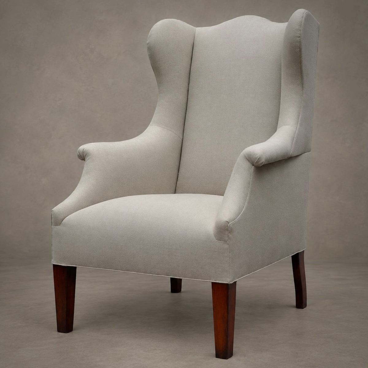 An upholstered wingback armchair with a light beige fabric and dark brown wooden legs, photographed against a neutral textured gray studio background.