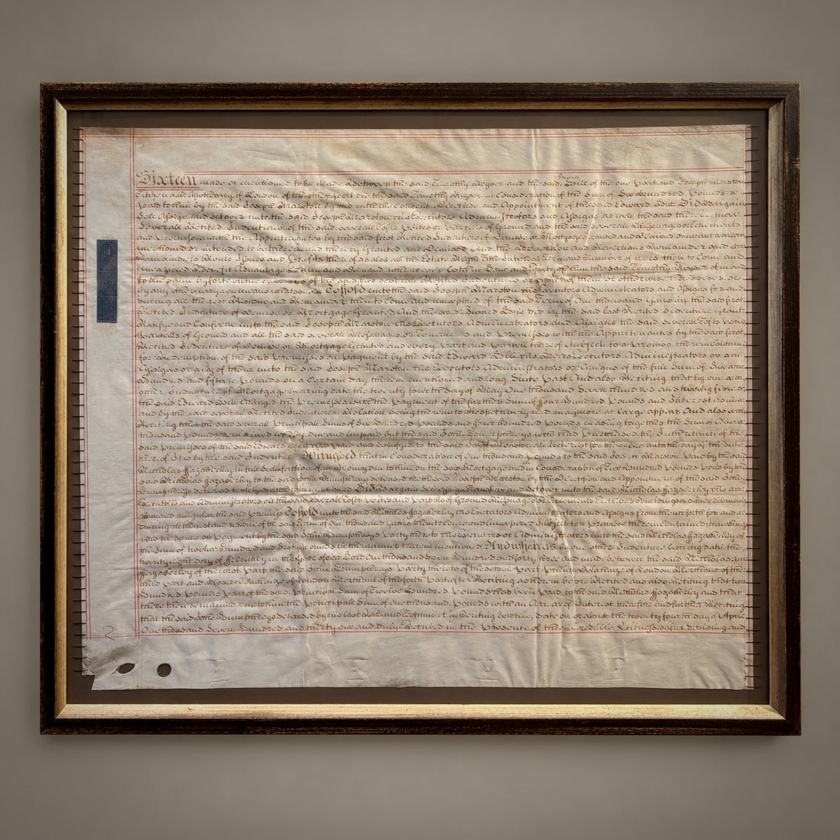 A framed historical manuscript or document with dense handwritten text, mounted on a light background and enclosed in a dark wood frame against a neutral gray wall.