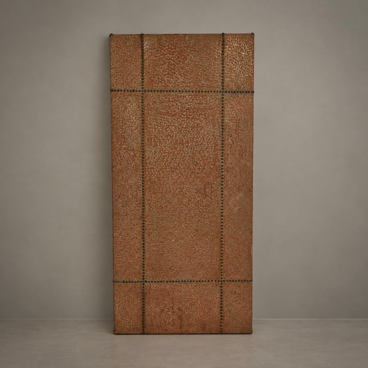 A tall rectangular brown textured panel with a stitched grid pattern and dark metal grommets, standing upright against a neutral gray wall.