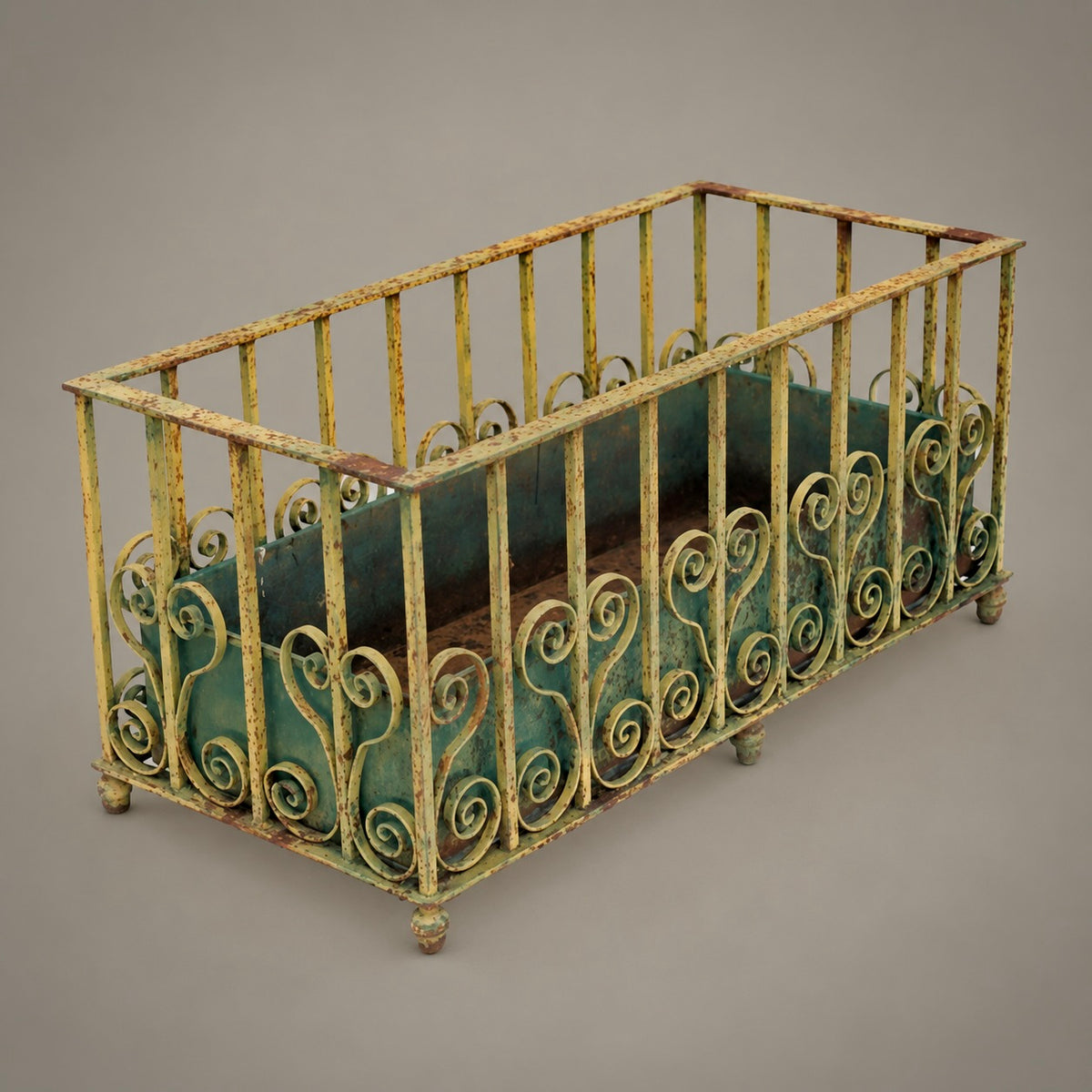 An antique-style rectangular metal crib or cage with ornate scrollwork on the front panels and a green interior lining, shown on a plain gray studio background.