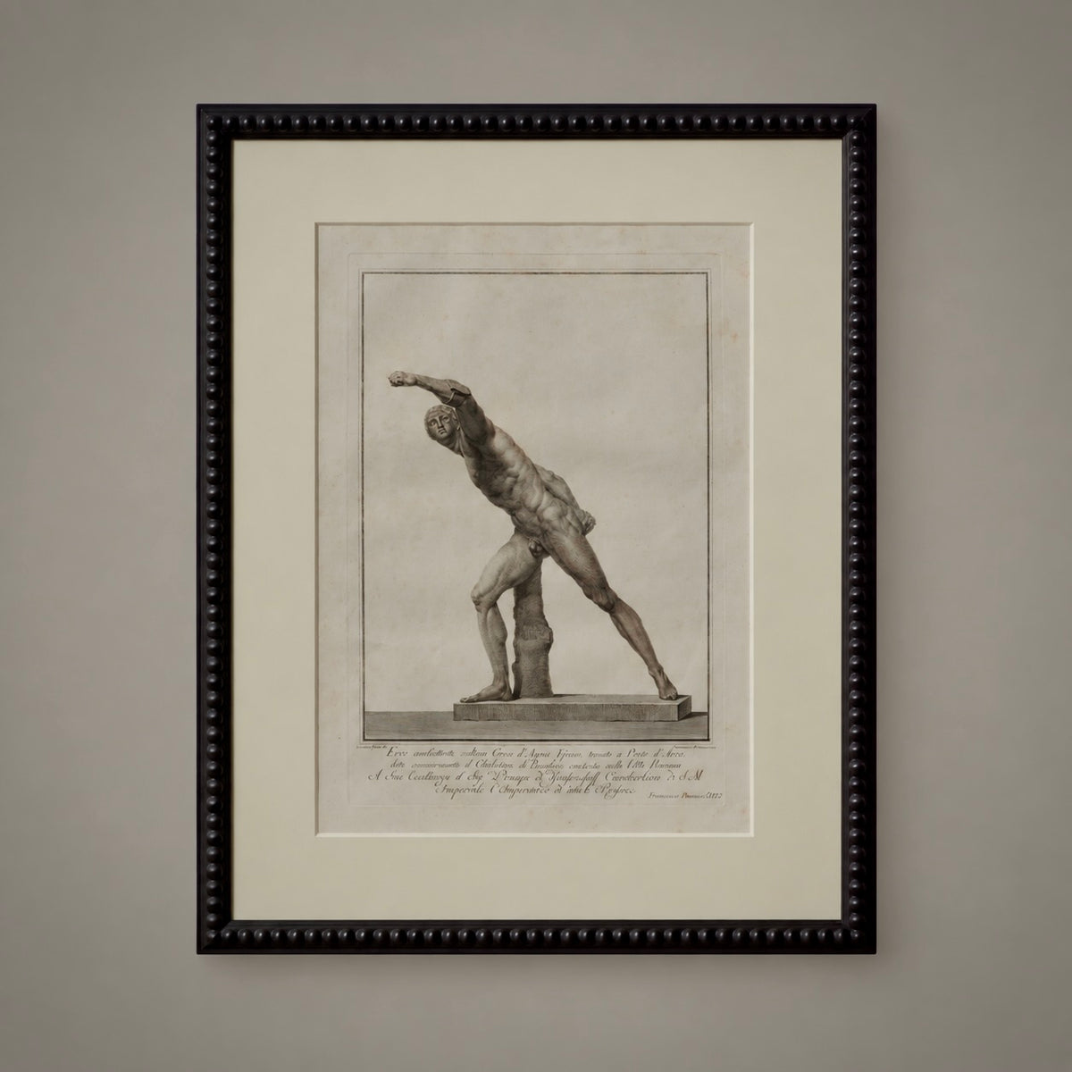 A framed classical art print featuring a sepia-toned sketch of a muscular male figure in a dynamic pose, mounted with a wide cream mat and a black beaded frame against a neutral gray wall.
